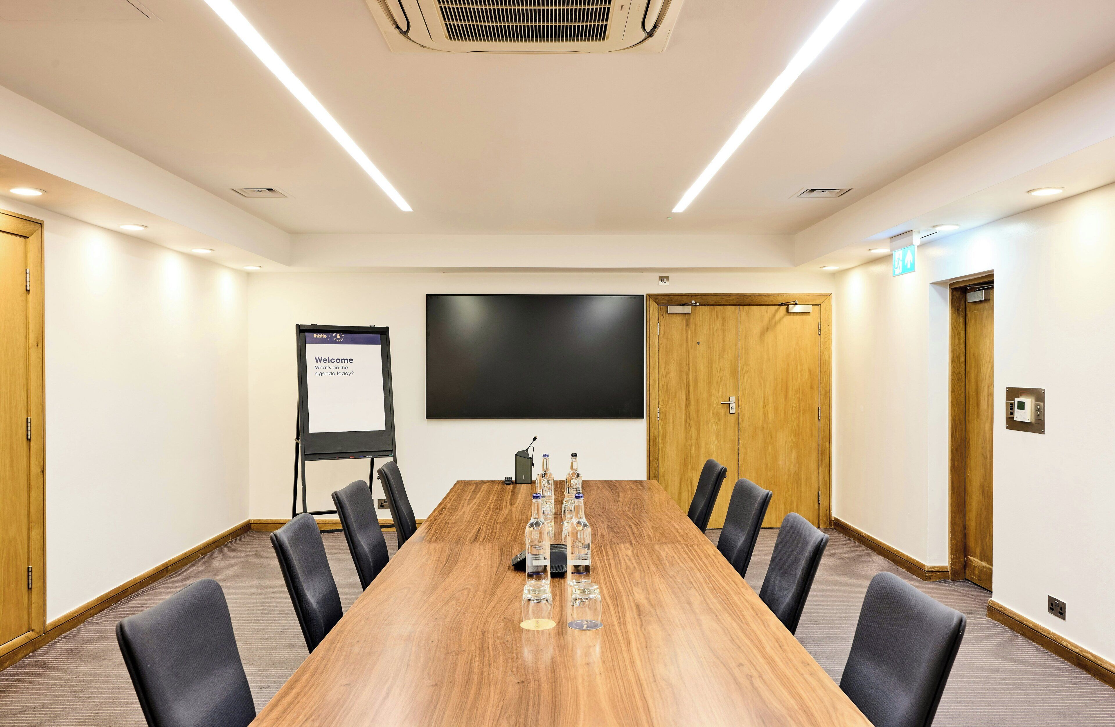 A conference room with a long wooden table, black chairs, a projector screen, and a whiteboard.