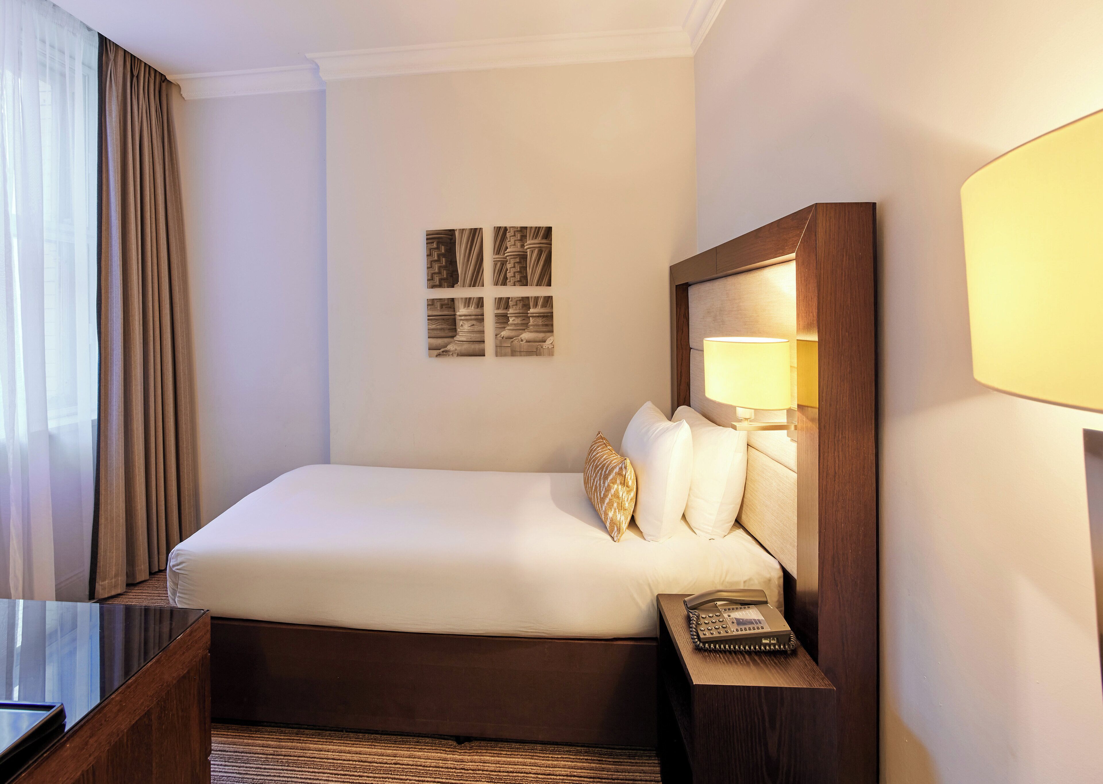 A hotel room with a large bed, a bedside table with a lamp, and a telephone.