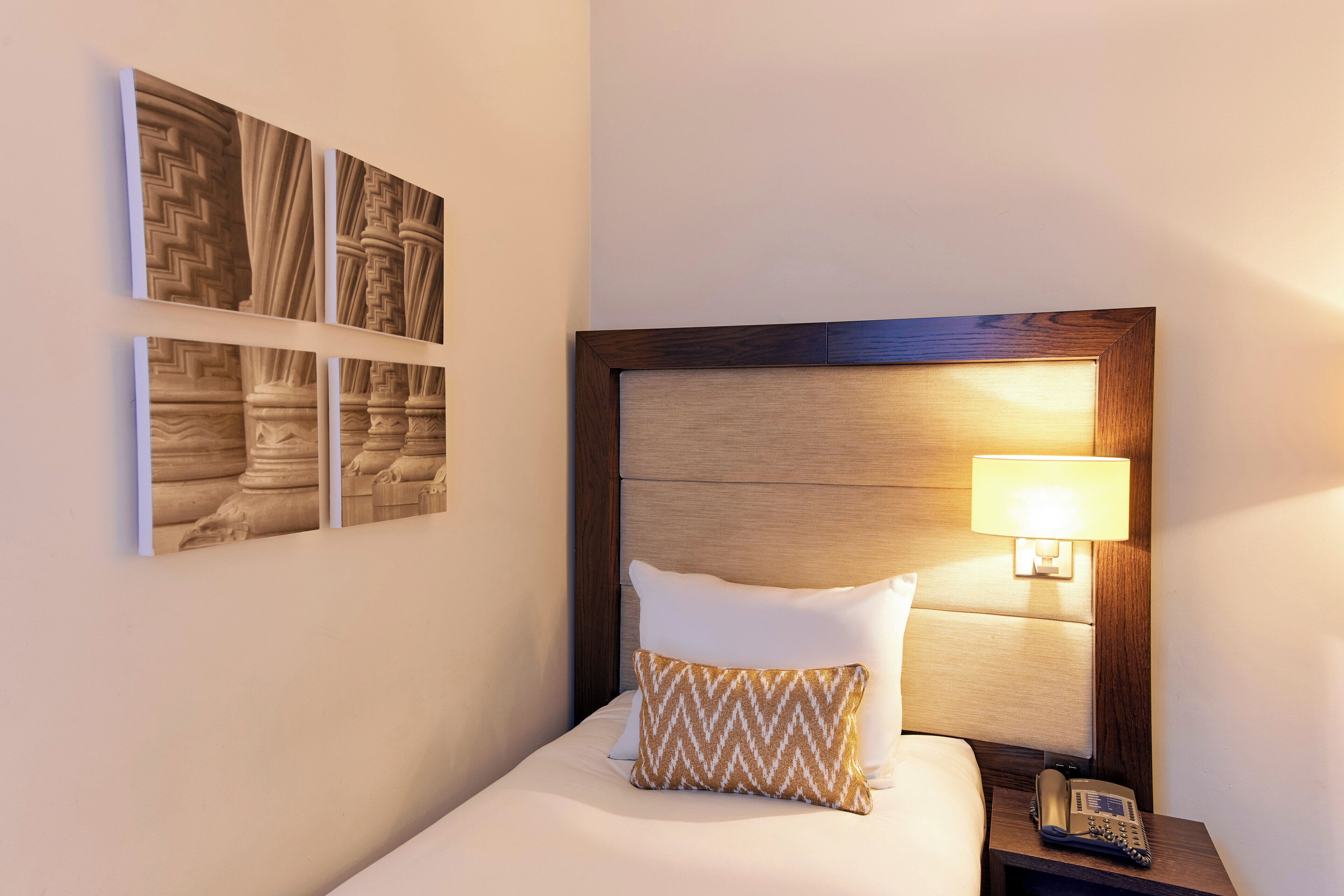 A neatly made bed with a wooden headboard, a bedside lamp, and a telephone on a nightstand.