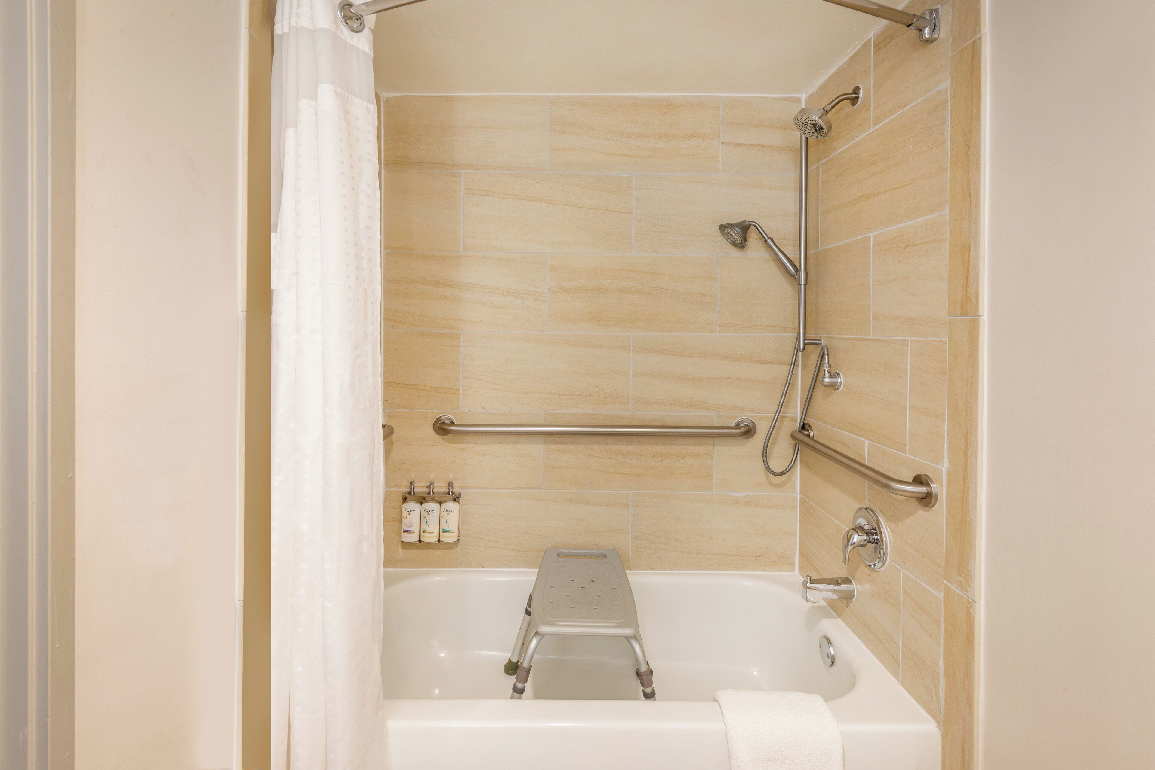 A bathroom with a bathtub, grab bars, a showerhead, and toiletries.