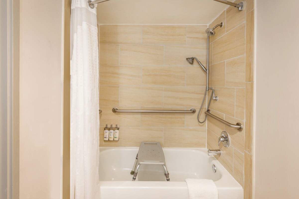 A bathroom with a bathtub, grab bars, and a shower chair.