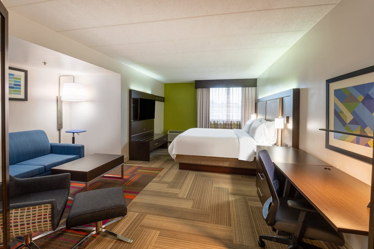A hotel room with a bed, a desk, a chair, a sofa, a TV, and a lamp.