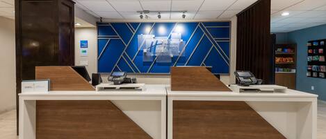 Un mostrador de recepción con dos áreas de servicio, una pared azul con el letrero de Holiday Inn Express, y una exhibición de servicios.