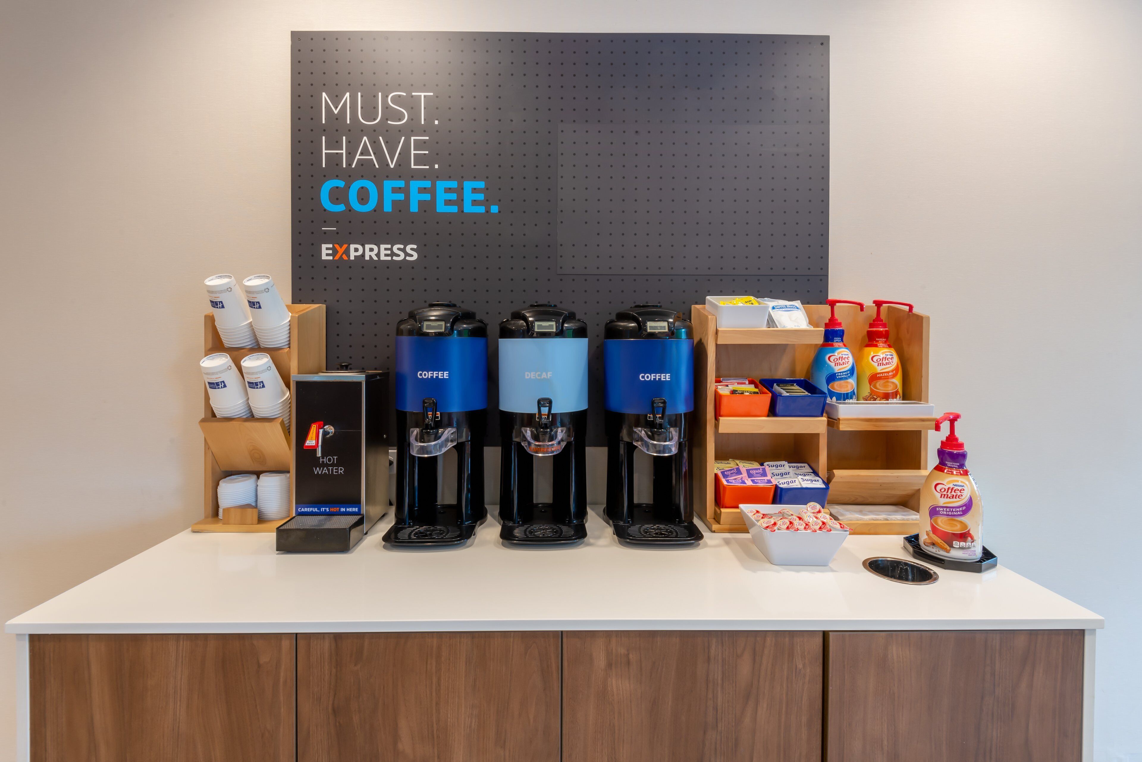 En kaffestation med flera kaffedispensrar, en skylt med texten ”KAFFE ÄR ETT MÅSTE” och diverse produkter relaterade till kaffe.