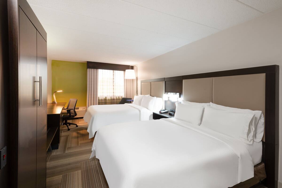 A hotel room with two beds, a desk, a chair, and a lamp.