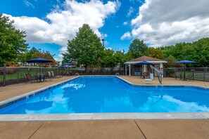 A rectangular swimming pool with a tiled edge, surrounded by a concrete deck. There are lounge chairs and umbrellas, and a covered seating area with a roof. - Holiday Inn Express Philadelphia NE - Bensalem by IHG (Bensalem)