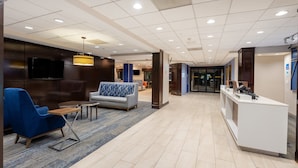A hotel lobby with a reception desk, seating area with sofas, a television mounted on the wall, and a patterned carpet. - Holiday Inn Express Philadelphia NE - Bensalem by IHG (Bensalem)