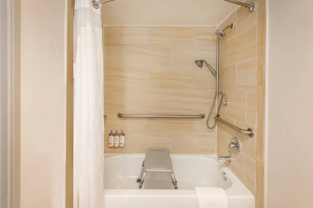 A bathroom with a bathtub, grab bars, and a shower chair.