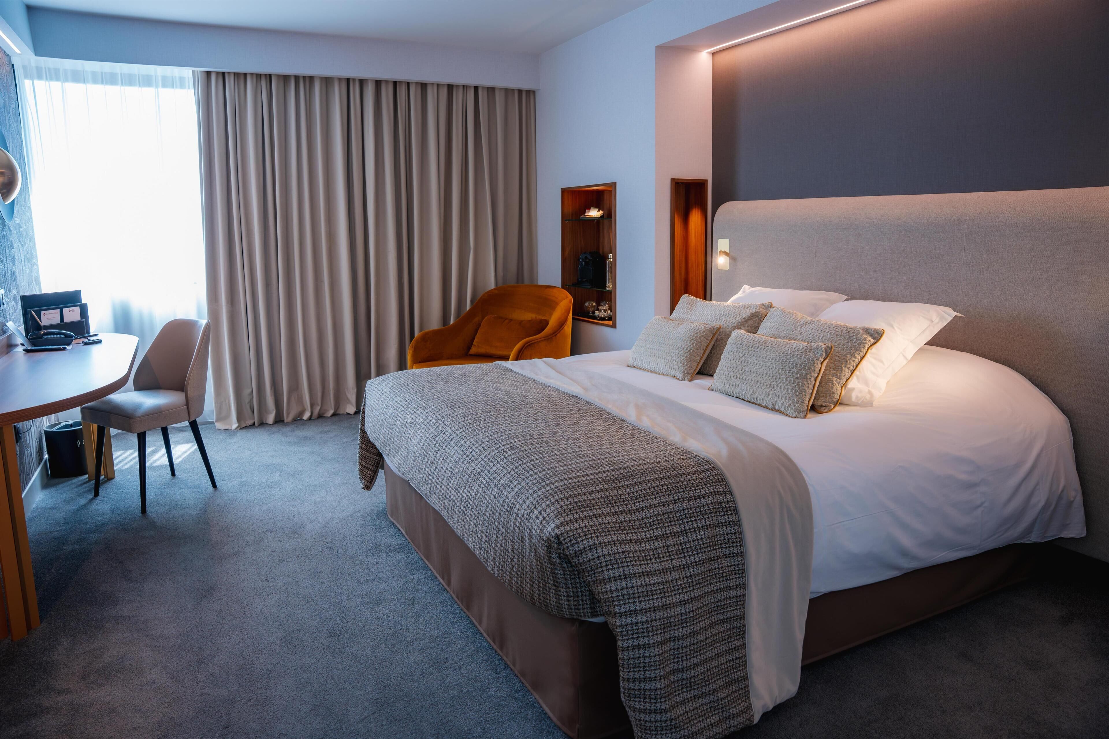 Habitación de hotel con cama, escritorio, silla y ventana con cortinas.