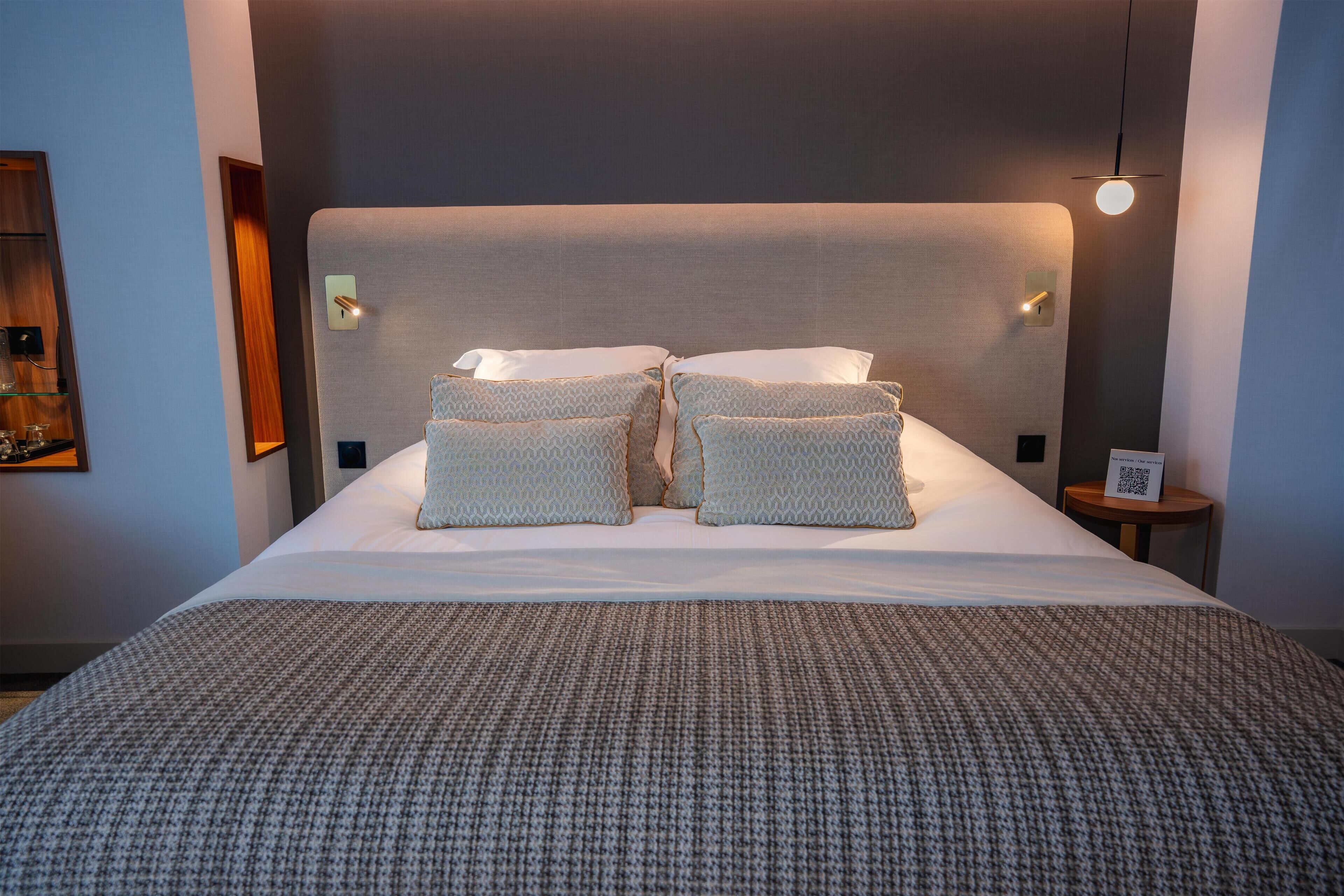 A neatly made bed with a grey headboard, two pillows, and a grey blanket.