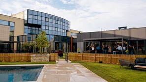 A modern building with a glass facade, a pool, and a wooden fence. - Best Western Plus Hotel Metz Technopole (Metz)