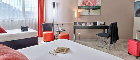A hotel room with a bed, a desk, a chair, a lamp, and a painting on the wall.