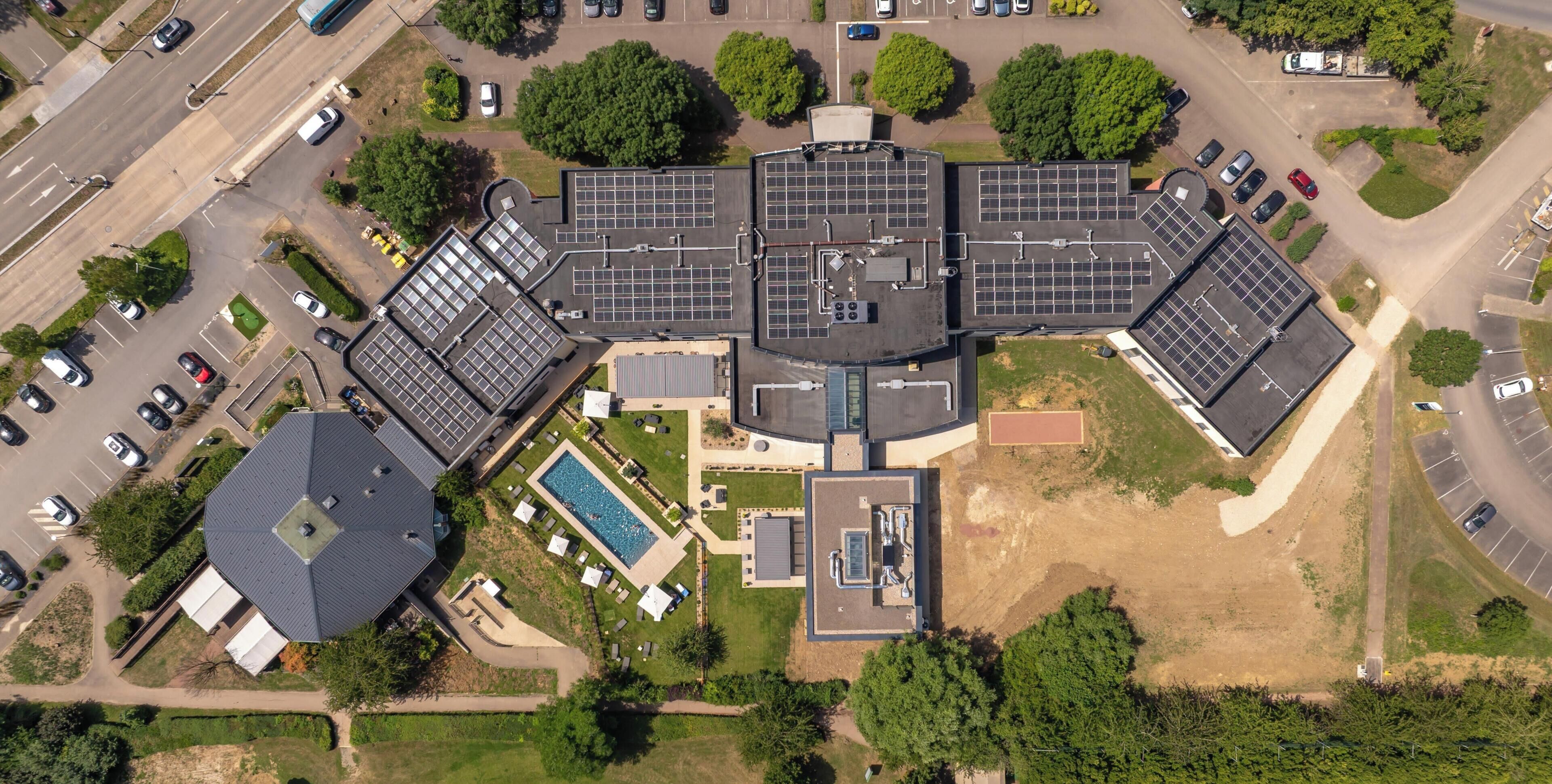 An aerial view of a building with multiple parking spaces, a swimming pool, and solar panels.