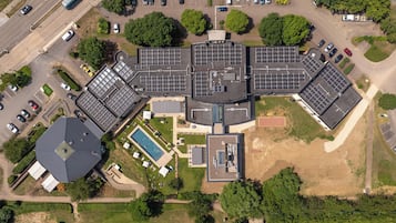 An aerial view of a building with multiple parking spaces, a swimming pool, and solar panels.