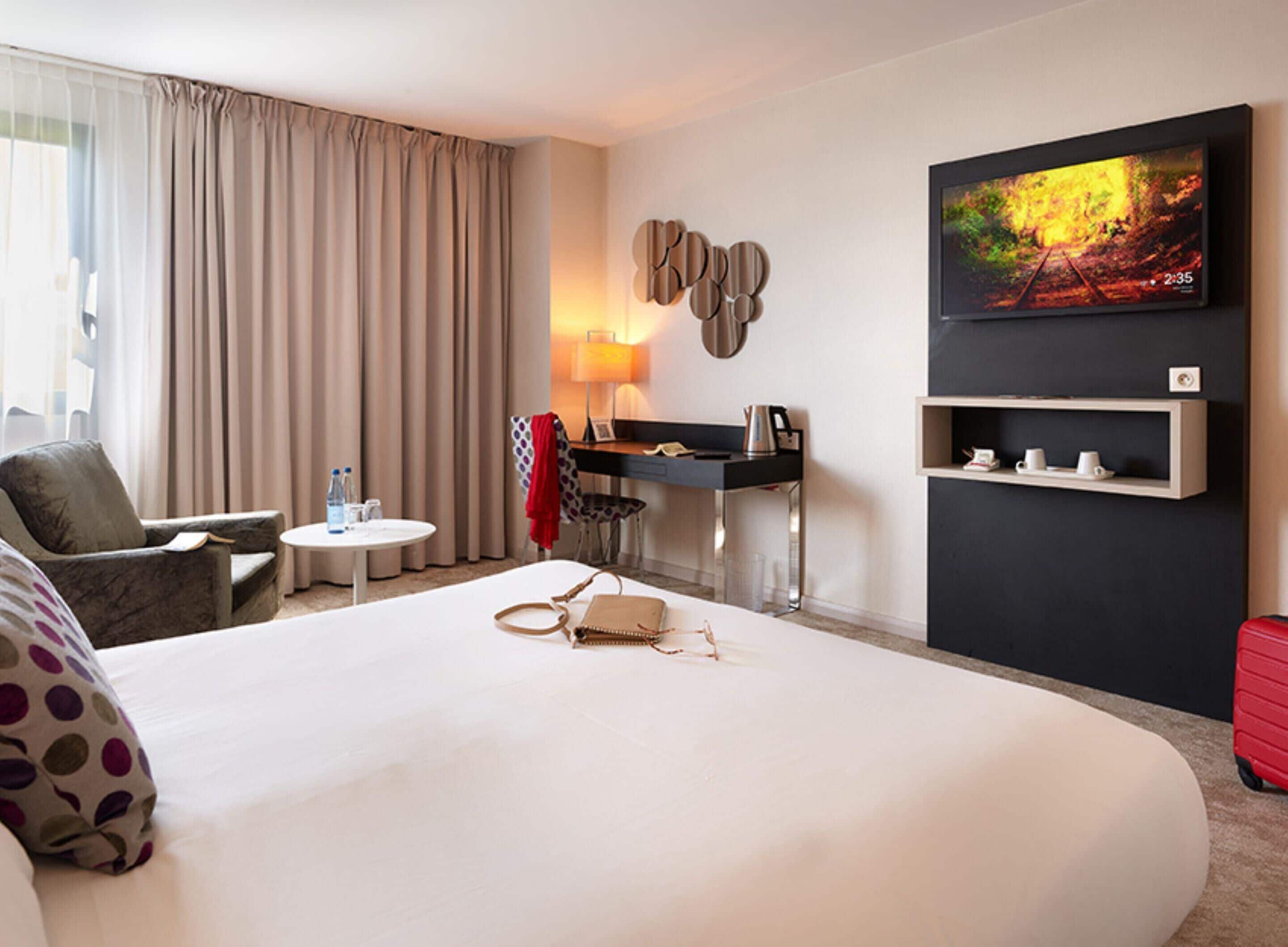 Habitació d'hotel amb un llit gran, un escriptori amb una cadira, una televisió i una estant amb gots.