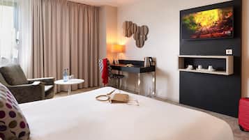 Hotelkamer met een groot bed, een bureau met stoel, een televisie en een plank met kopjes.