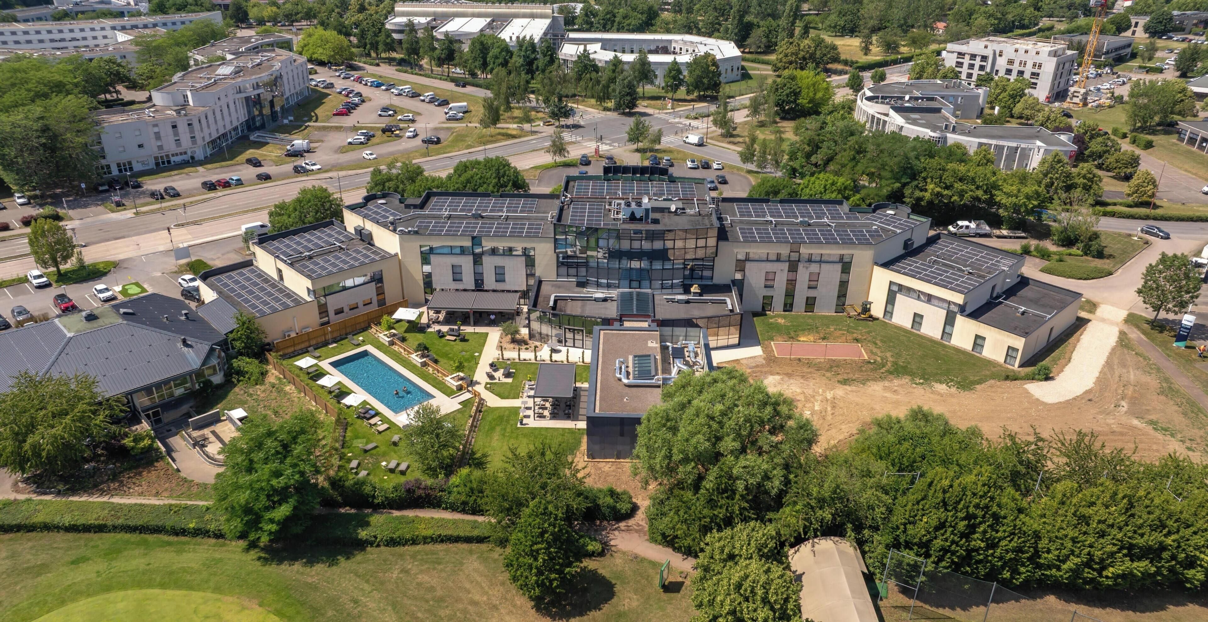 Vista aérea de un moderno complejo de edificios con varias construcciones, una piscina y zonas verdes circundantes.