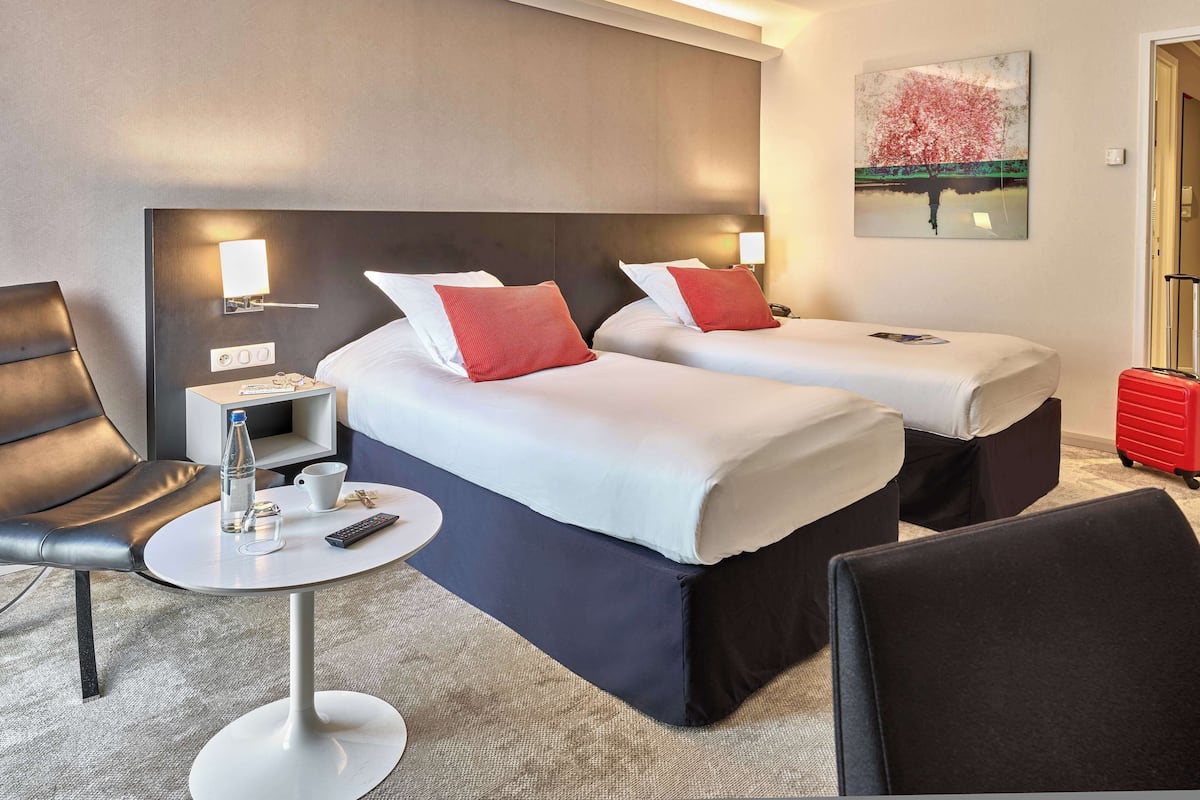 A hotel room with two beds, a desk, a chair, and a painting on the wall.