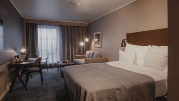 A hotel room with a bed, a desk, a chair, a sofa, and a window with curtains.