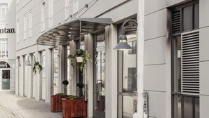 Un hotel con fachada moderna, entrada cubierta y plantas colgantes.