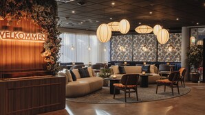 Una zona de recepción moderna con un mostrador de madera, asientos cómodos y plantas decorativas.