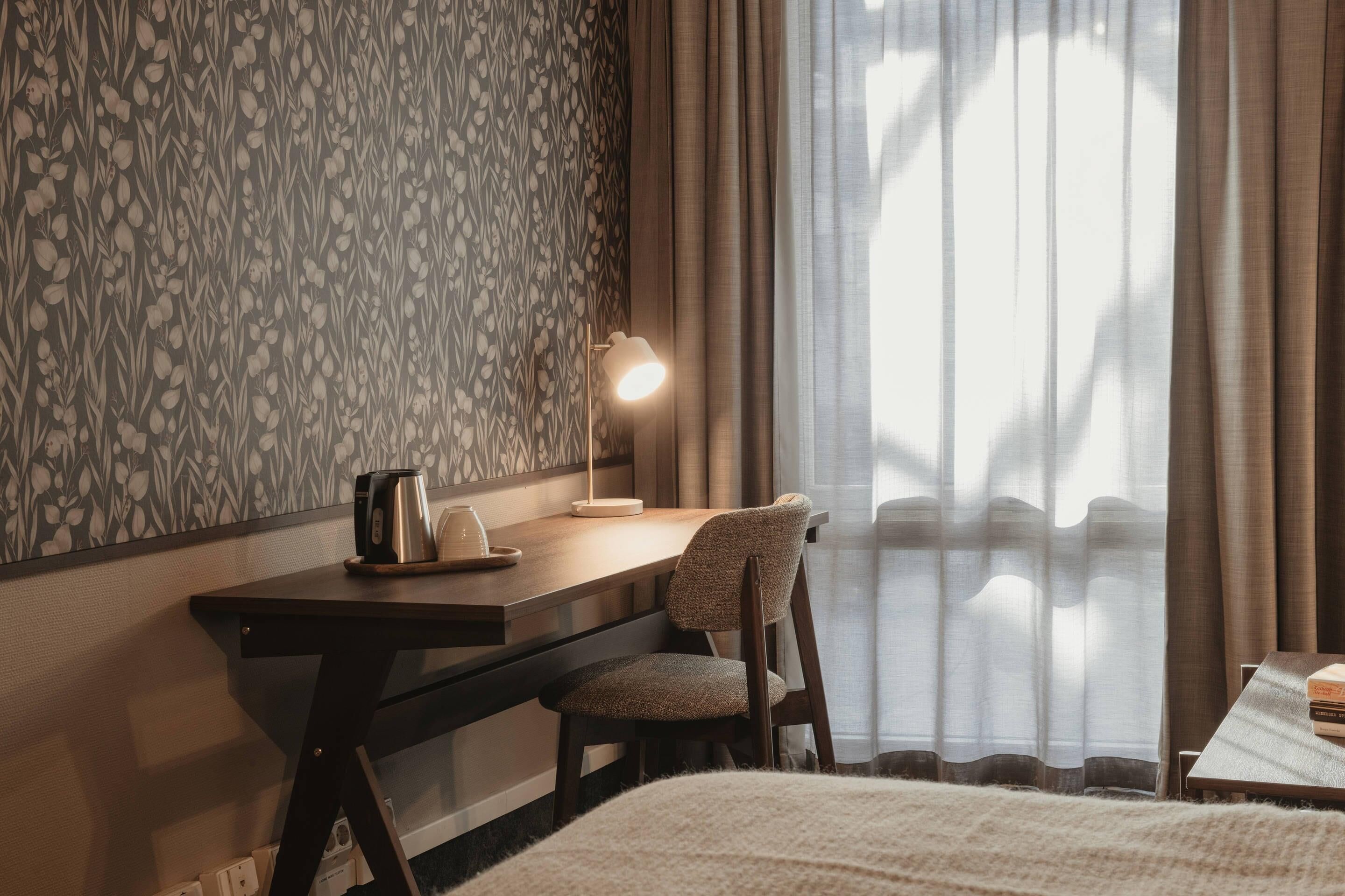 A hotel room with a desk, chair, and a bed.