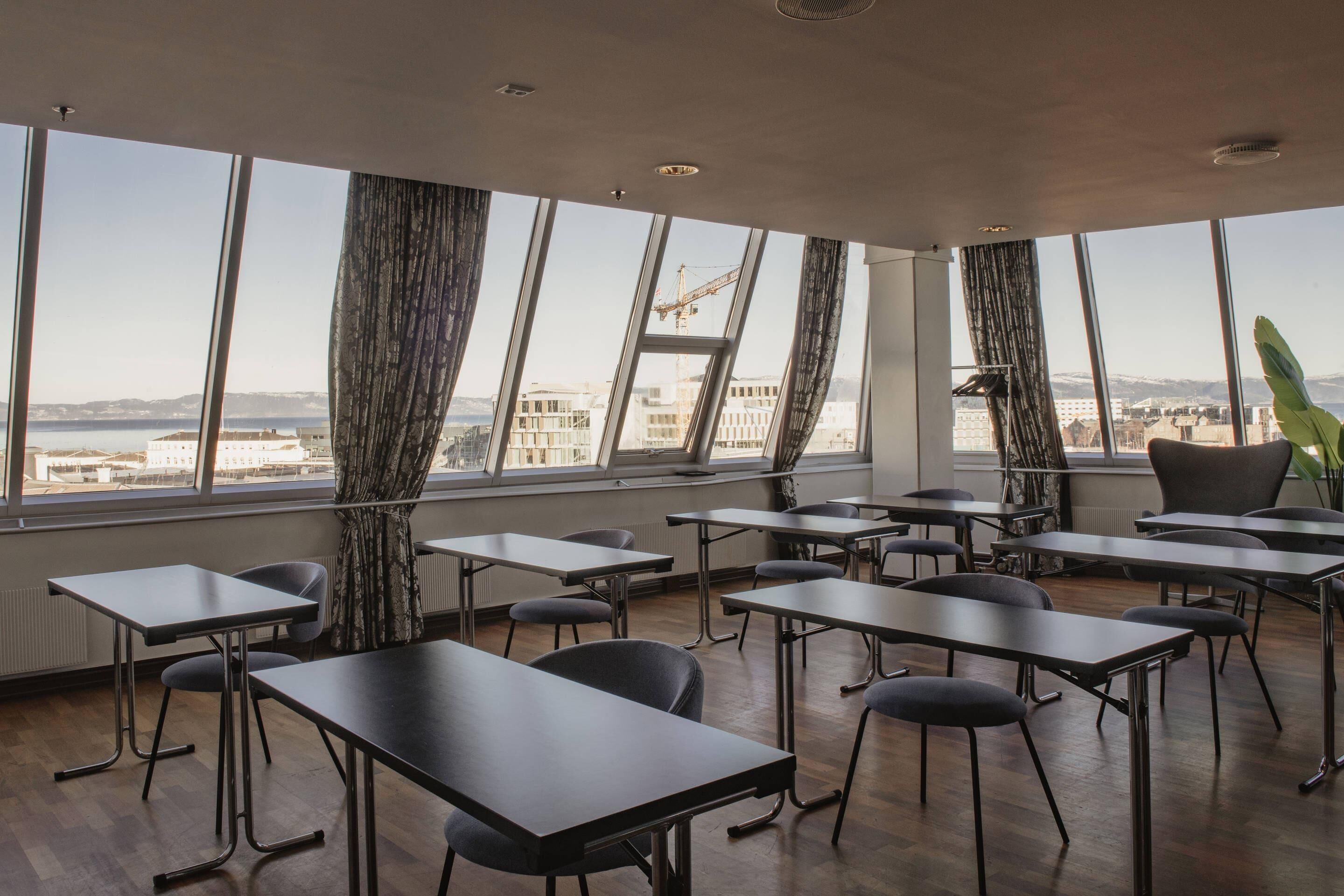 Una sala conferenze moderna con ampie finestre, diversi tavoli e sedie disposte per riunioni.