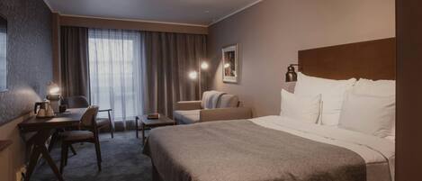 A hotel room with a bed, a desk with a chair, a sofa, and a window with curtains.