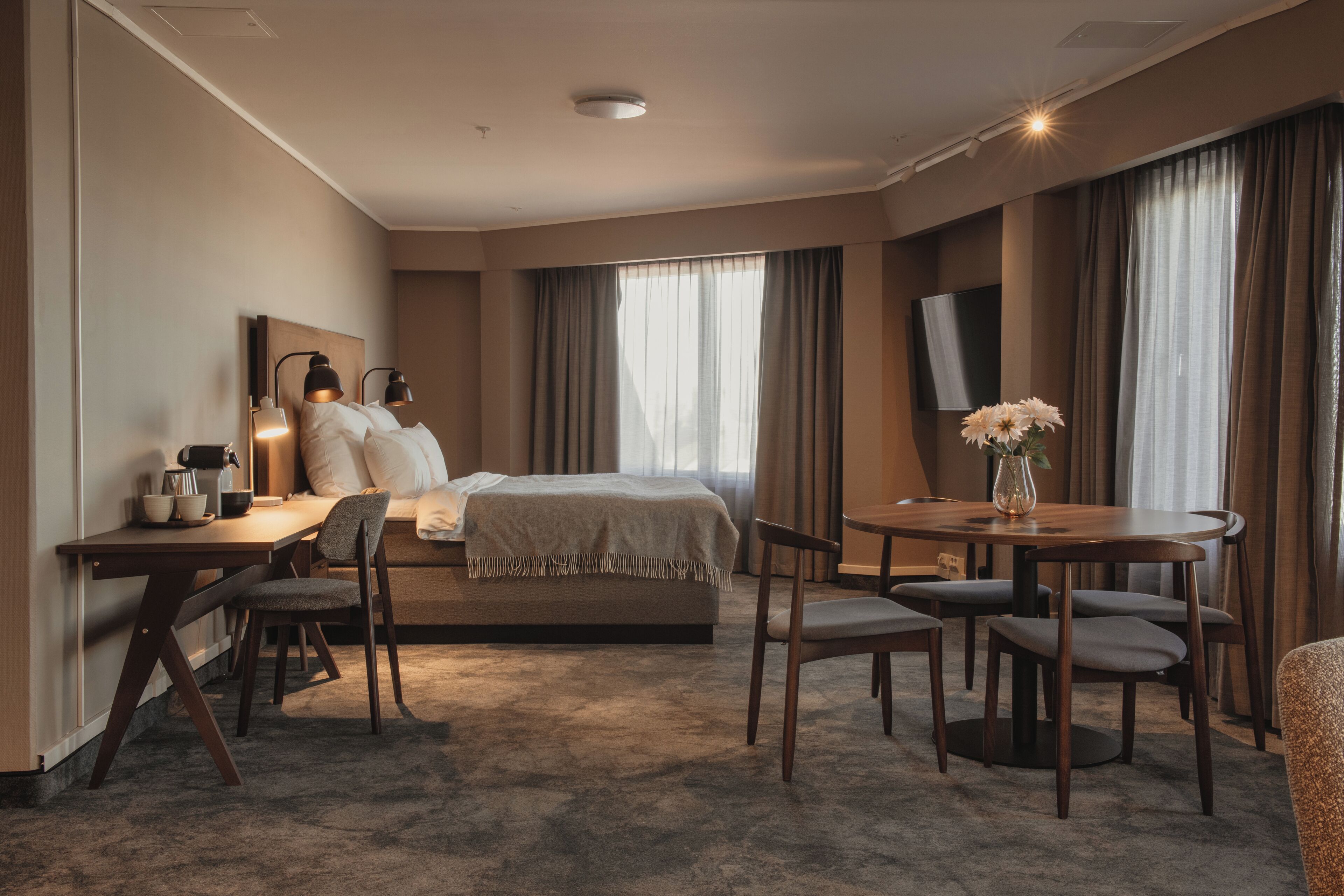 Habitación de hotel con cama, mesita de noche, lámpara, silla, escritorio, mesa de comedor y televisor de pantalla plana.