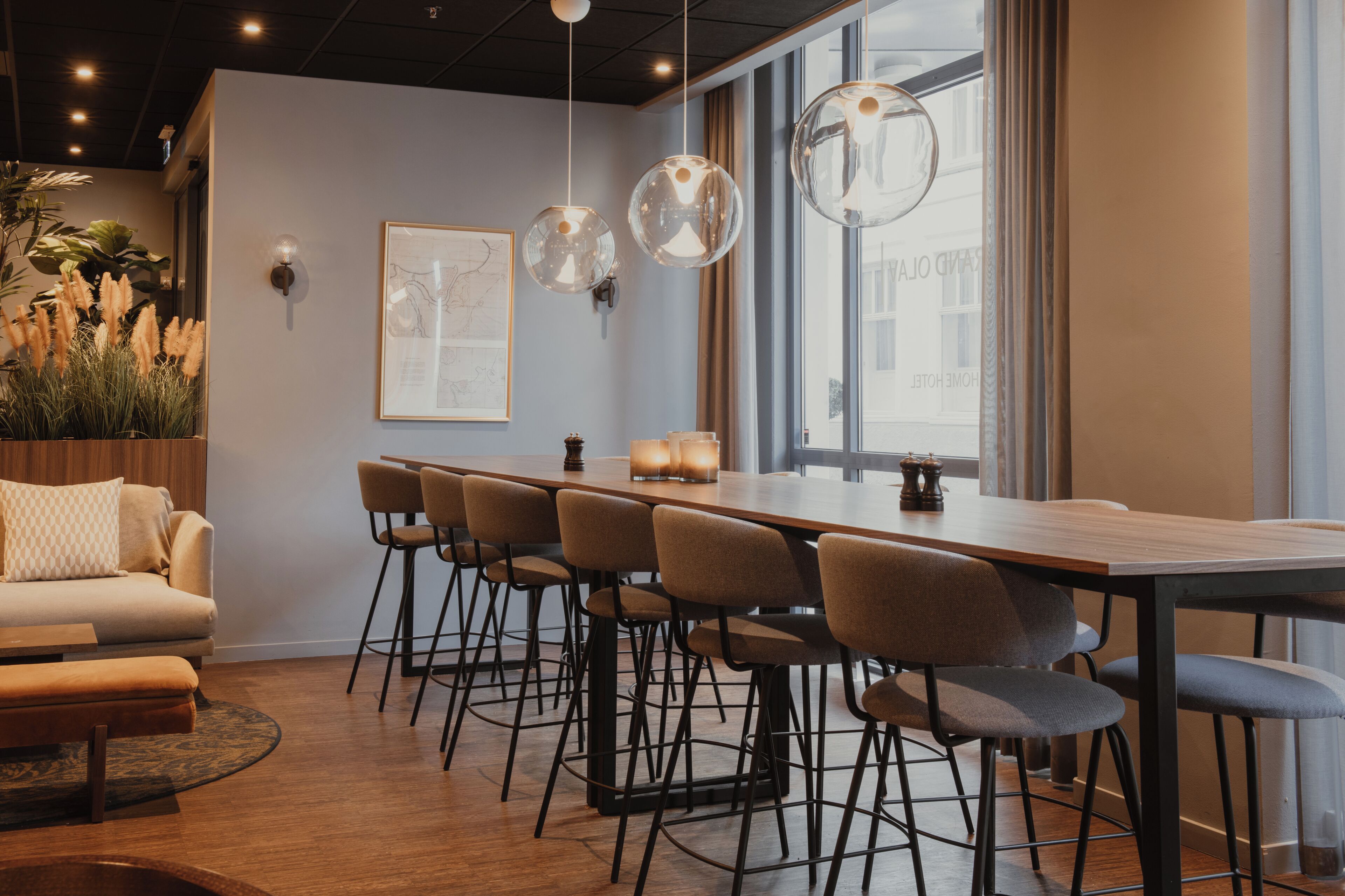 Un área de comedor moderna con una mesa larga, taburetes de bar, iluminación colgante y un sofá.