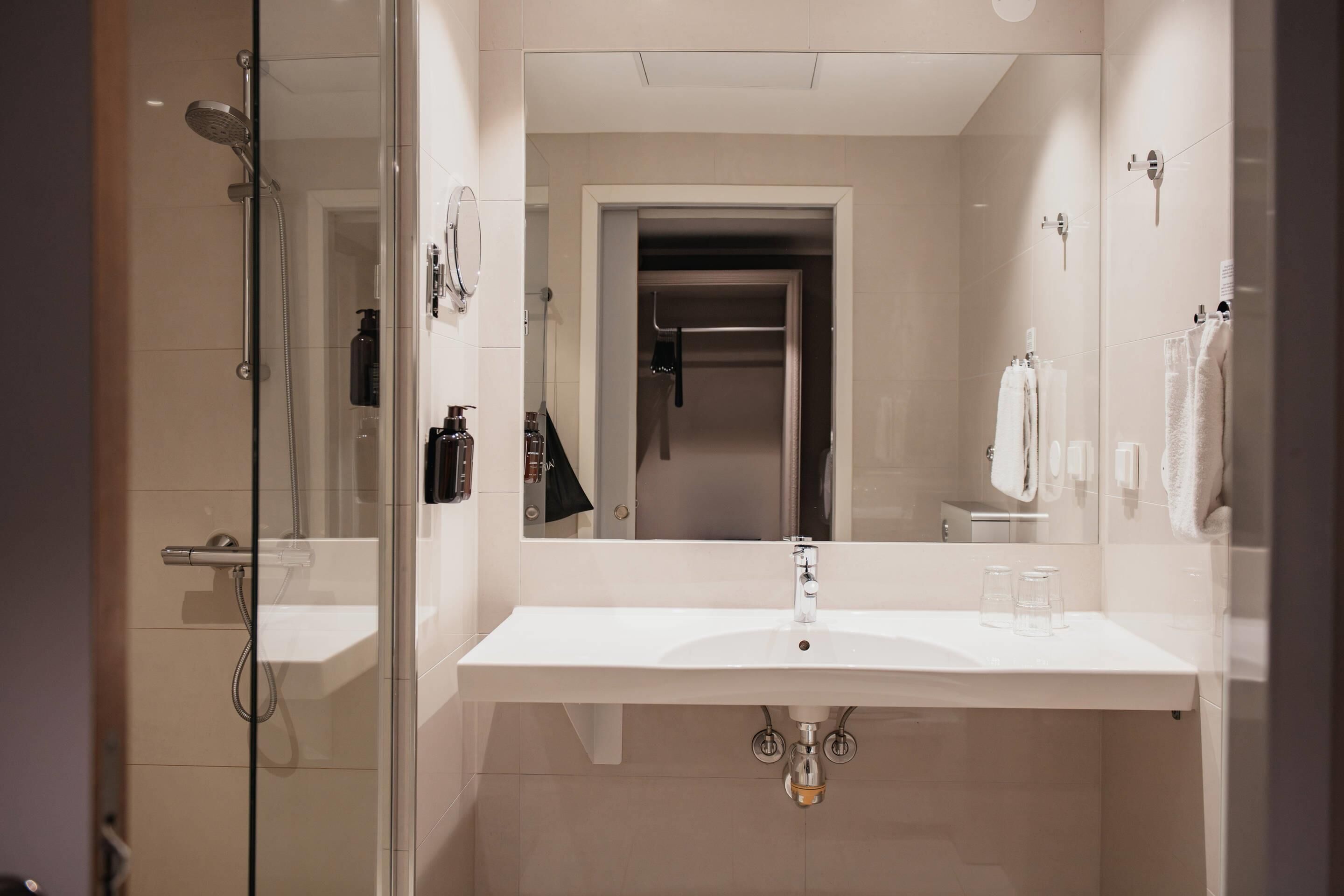 Un baño moderno con ducha acristalada, un lavabo blanco y un espejo encima.