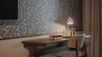 A room with a patterned wallpaper, a wooden desk, a chair, a lamp, and a few books.