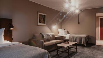 A hotel room with a sofa, two single beds, a small table, and a framed picture on the wall.