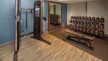 A gym with a weight bench, a squat rack, and a wall of dumbbells.