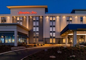 A Hampton Inn hotel with a modern facade, large windows, and a well-lit entrance.