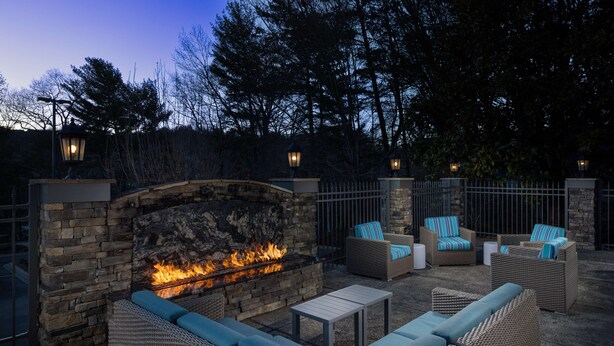 An outdoor patio with a stone fireplace, wicker furniture, and a stone wall. - Hampton Inn Asheville-Tunnel Rd. (Asheville)