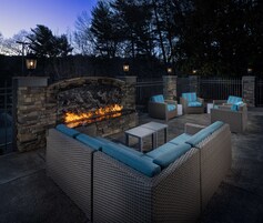 An outdoor patio with a stone fireplace, wicker furniture, and a stone wall.