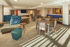 A modern hotel lobby with seating areas, a bar, and a flat-screen TV.