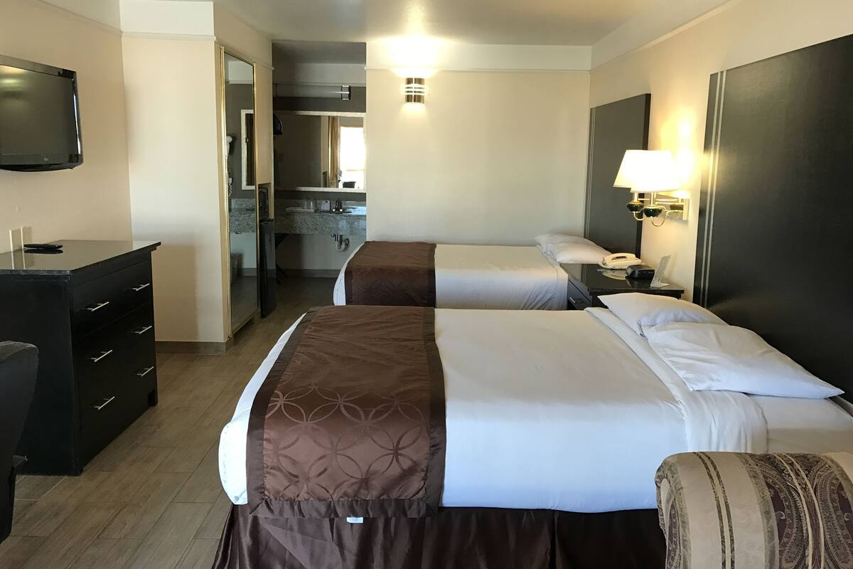A hotel room with two beds, a desk, a television, and a kitchenette.