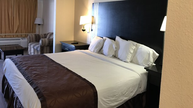 A hotel room with a large bed, a desk, a chair, and a lamp. - Texas Inn & Suites (Pharr)