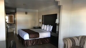 A hotel room with a bed, a desk, a chair, a sofa, a bathroom, and a mirror. - Texas Inn & Suites (Pharr)