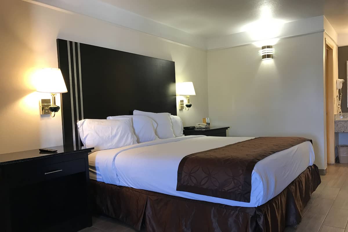 A hotel room with a large bed, two bedside tables, a black headboard, and two wall-mounted lamps.