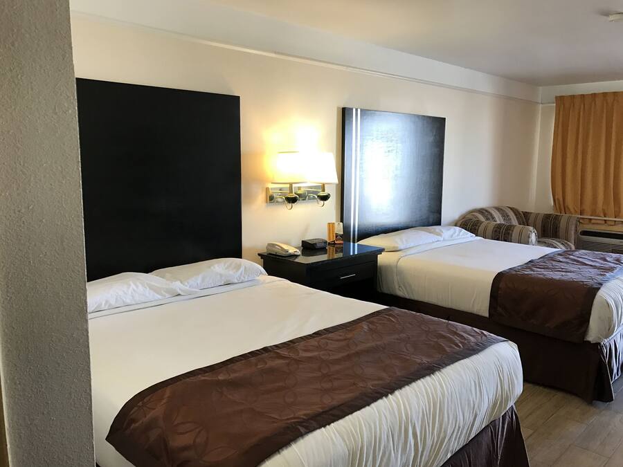 A hotel room with two beds, a large mirror, a bedside table with a lamp, and a window with curtains.