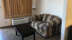 A living room with a sofa, a table, a window with curtains, and an air conditioning unit. - Texas Inn & Suites (Pharr)
