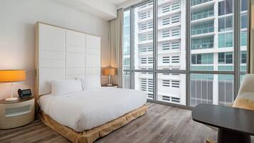 A modern hotel room with a large bed, bedside tables, a desk, and a large window with a city view.