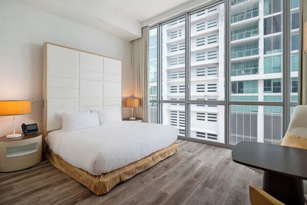 A modern hotel room with a large bed, bedside tables, a desk, and a large window with a city view. - The Grayson Miami Downtown (Miami)