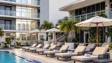 A poolside area with lounge chairs and umbrellas, a clear pool, and a modern building with large windows.