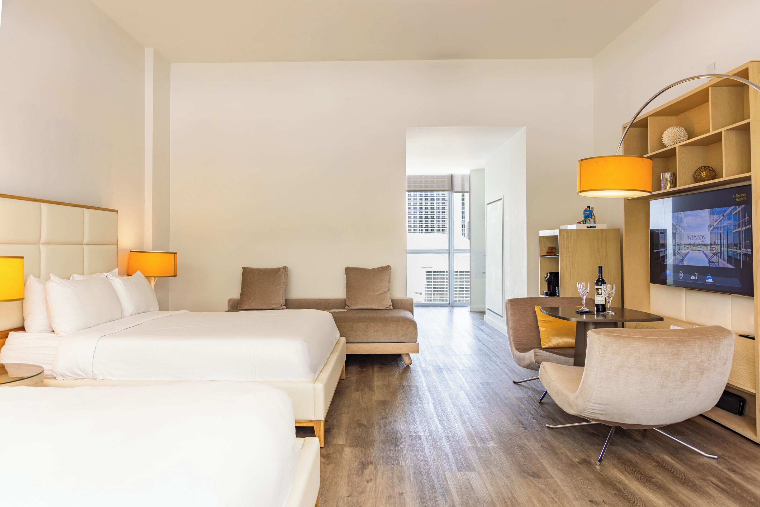 A hotel room with two beds, a sofa, a dining table, and a TV.