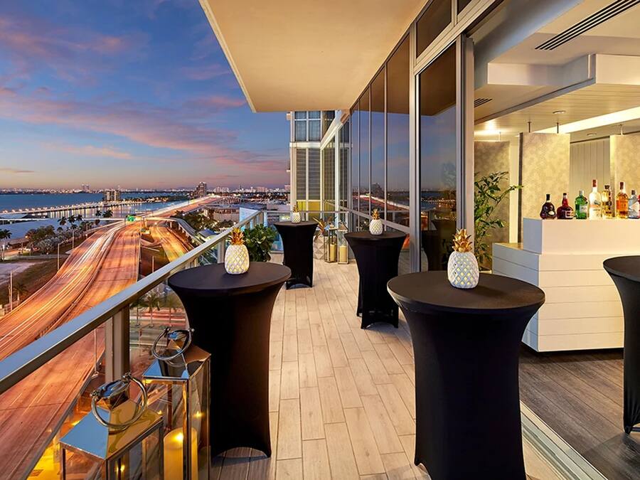 Un balcón con vistas a la ciudad, mesas, sillas y una zona de bar.