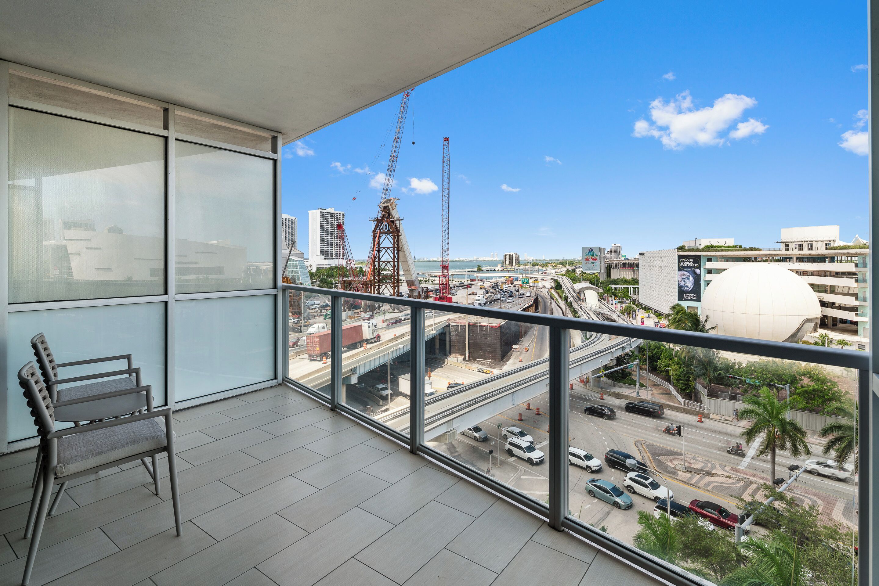 A balcony with a view of a busy street, construction cranes, and a large spherical building.